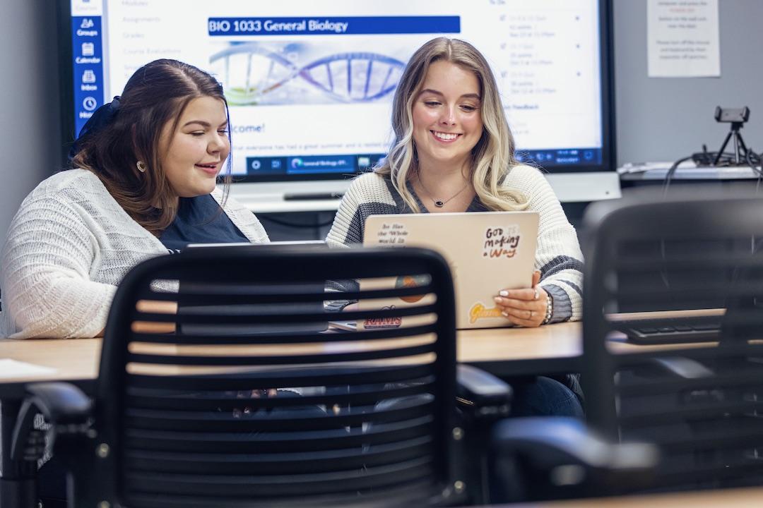 Two female students use an iPad and a laptop in Easley Library.